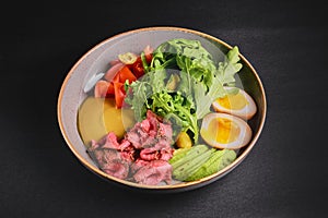 Carpaccio with with boiled eggs, avocado, fresh tomatoes and arugula in a plate over black background.