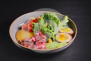 Carpaccio with with boiled eggs, avocado, fresh tomatoes and arugula in a plate over black background.