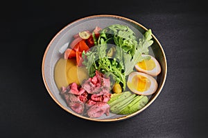 Carpaccio with with boiled eggs, avocado, fresh tomatoes and arugula in a plate over black background.