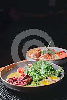 Carpaccio with with boiled eggs, avocado, fresh tomatoes and arugula in a plate over black background.