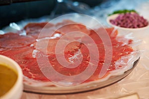 Carpaccio, closeup and food on plate for dinner with appetizer, fine dining and buffet of raw meat in restaurant. Beef