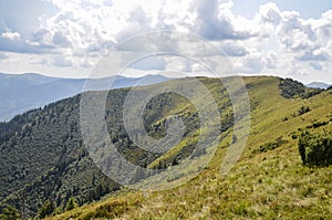 Carpathian Mountains with its peaks, hills and grassy meadows under the blue sky with clouds in summer day