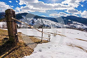 carpathian rural landscape in winter. wooden fence on the snow covered hill. village in the distant valley. bright sunny day with