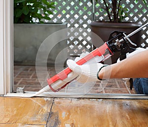 Carpenter applies silicone caulk on the wooden floor for sealing photo