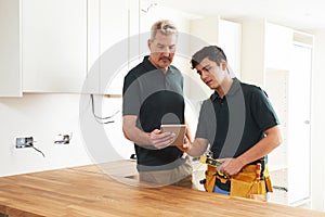 Carpenter And Apprentice With Digital Tablet Fitting Luxury Kitchen