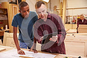 Carpenter With Apprentice Looking At Plans In Workshop