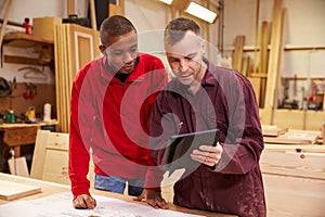 Carpenter With Apprentice Looking At Plans In Workshop