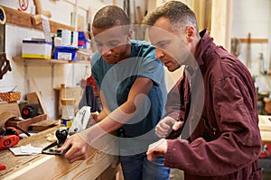 Carpenter With Apprentice Planing Wood In Workshop