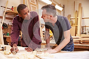 Carpenter With Apprentice Planing Wood In Workshop