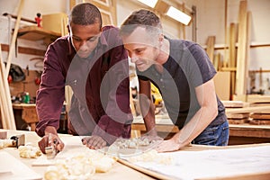 Carpenter With Apprentice Planing Wood In Workshop