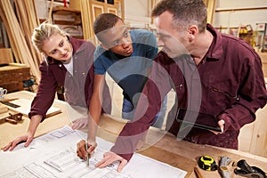 Carpenter With Apprentices Looking At Plans In Workshop