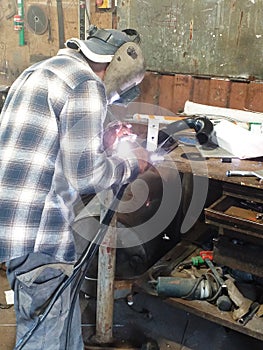 Carpenter from behind and with protective material working in carpentry workshop. Workbench, tools and old utensils in French West