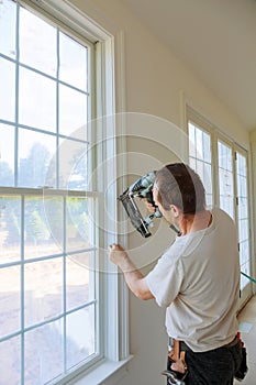 Carpenter brad using nail gun to moldings on windows, framing trim,