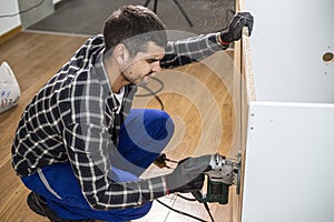 A carpenter with a corded jigsaw cutting a part of the wooden surface (board