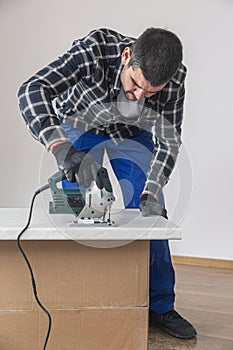 A carpenter with a corded jigsaw cutting a part of the wooden surface (board