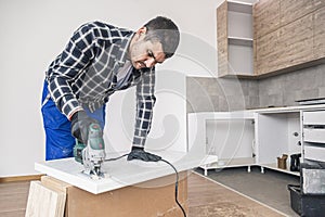 A carpenter with a corded jigsaw cutting a part of the wooden surface (board