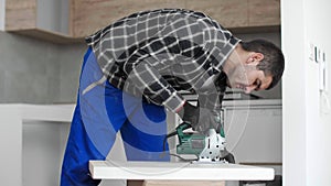 A carpenter with a corded jigsaw cutting a part of the wooden surface (board