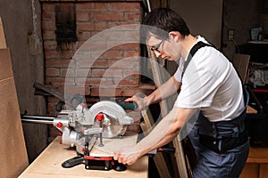 Carpenter cuts a piece of plywood with a miter saw photo