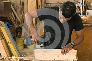 carpenter drilling a piece of wood with a drill. craft procedures with wood.