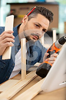 Carpenter with electric drill drilling wood plank
