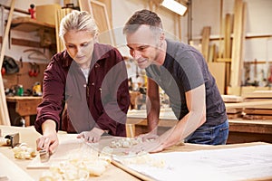 Carpenter With Female Apprentice Planing Wood In Workshop