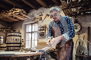 Carpenter in glasses uses jack-plane to smooth the surface of wood in the workshop