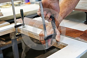 The carpenter glues pieces of furniture together and presses them down with clamps. Cropped frame. Close-up