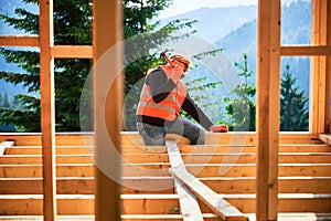 Carpenter hammering nail while constructing wooden frame two-story house near the forest.