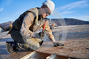 Carpenter hammering nail into OSB panel while building wooden frame house.