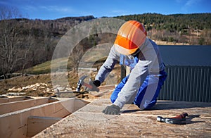 Carpenter hammering nail into OSB panel while building wooden frame house.