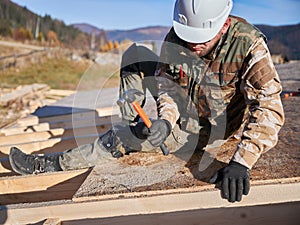 Carpenter hammering nail into OSB panel while building wooden frame house.