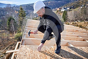 Carpenter hammering nail into OSB panel while building wooden frame house.