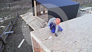 Carpenter hammering nail into OSB panel while building wooden frame house.