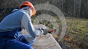 Carpenter hammering nail into OSB panel while building wooden frame house.