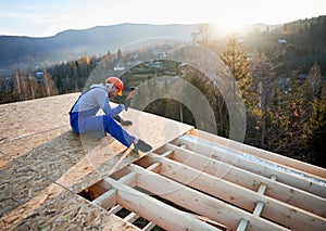 Carpenter hammering nail into OSB panel while building wooden frame house.