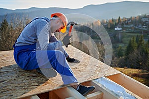 Carpenter hammering nail into OSB panel while building wooden frame house.