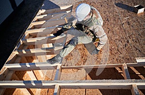 Carpenter hammering nail into OSB panel while building wooden frame house.