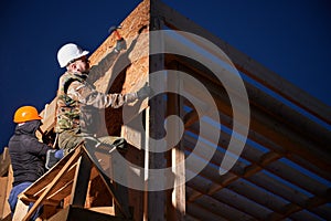 Carpenter hammering nail into OSB panel while building wooden frame house.