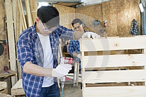 Carpenter hammering nails into wood with a automatic nailer. Carpenter worker with machine at wood workshop photo