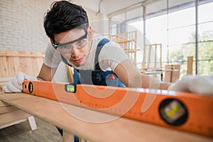 Carpenter handsome man wearing goggle and gloves with using water level for height checking of desk in workplace at home