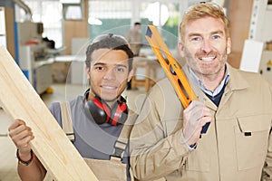 carpenter holding spirit level with apprentice in workshop
