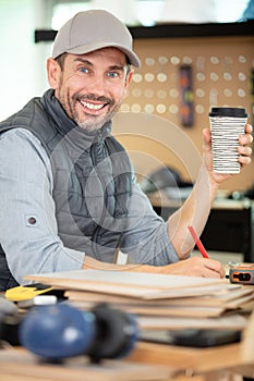 carpenter holds coffee while working in carpentry workshop