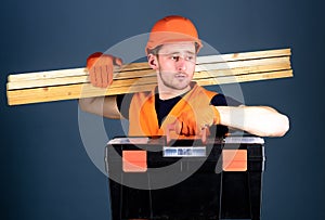 Carpenter, labourer, builder, woodworker on calm face carries wooden beams on shoulder. Man in helmet, hard hat holds
