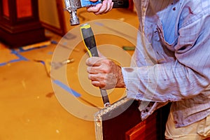Carpenter makes a hole in wooden door for the mortise lock with a hammer and chisel.