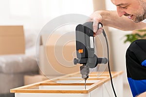 Carpenter Making Furniture Using Electric Drill Assembling Shelf Indoors