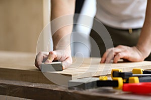 Carpenter man grinds wooden sheet in workshop