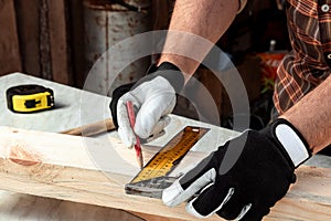 Carpenter man notes with a pencil on the board marks for cutting, male hands with a pencil closeup on a wooden board. Woodwork