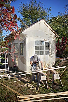 Carpenter Man Using Circular Saw Building a Small Garden Cottage Shed