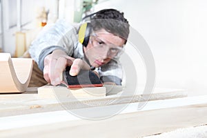 Carpenter man work in the carpentry, sanding wooden boards with sandpaper, protected with ear muffs