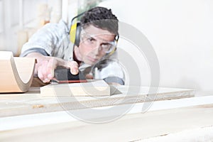 Carpenter man work in carpentry, sanding wooden boards with sandpaper, protected with ear muffs and glasses